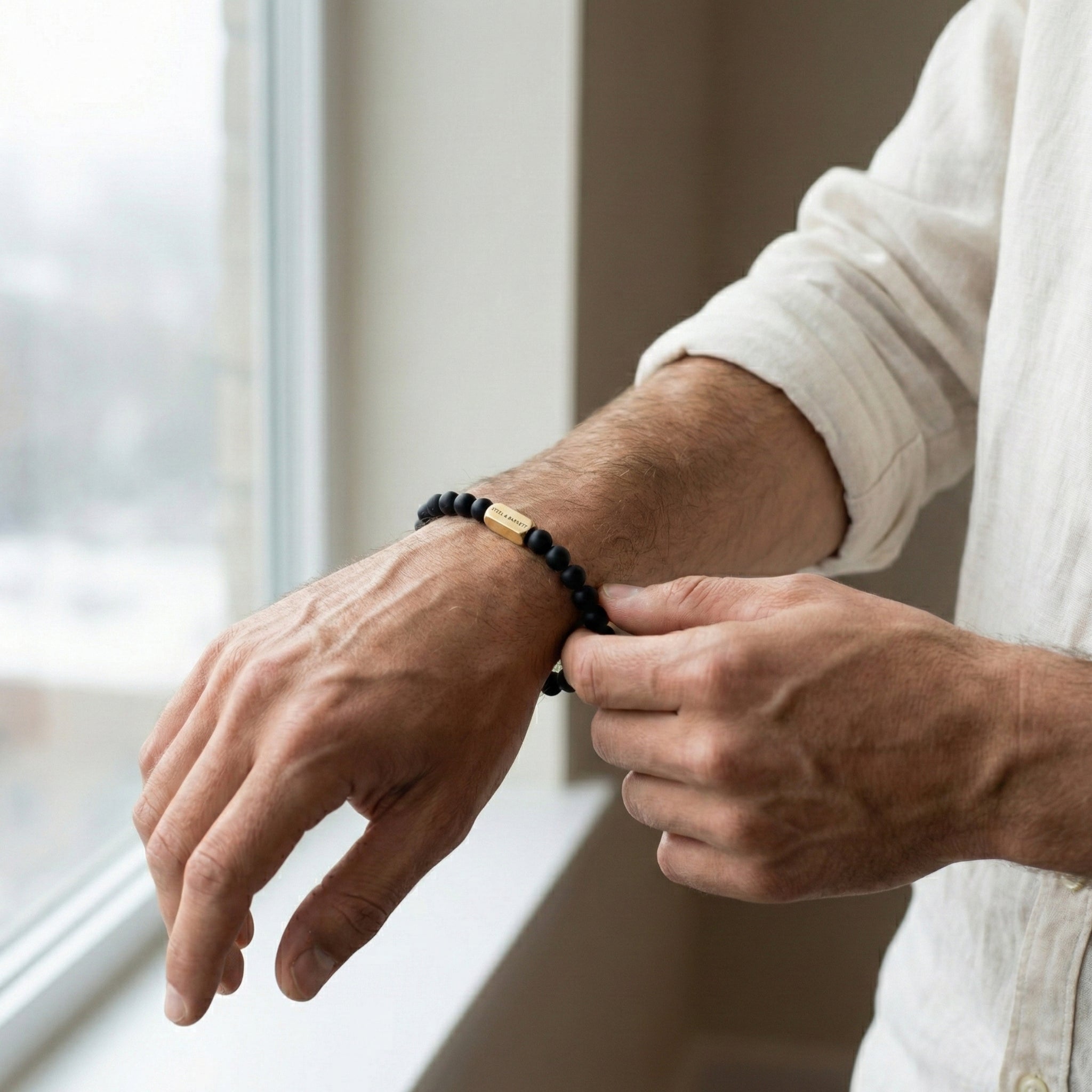 Black beaded men’s bracelet with matte beads and plated 18K gold clasp on dark stone surface
