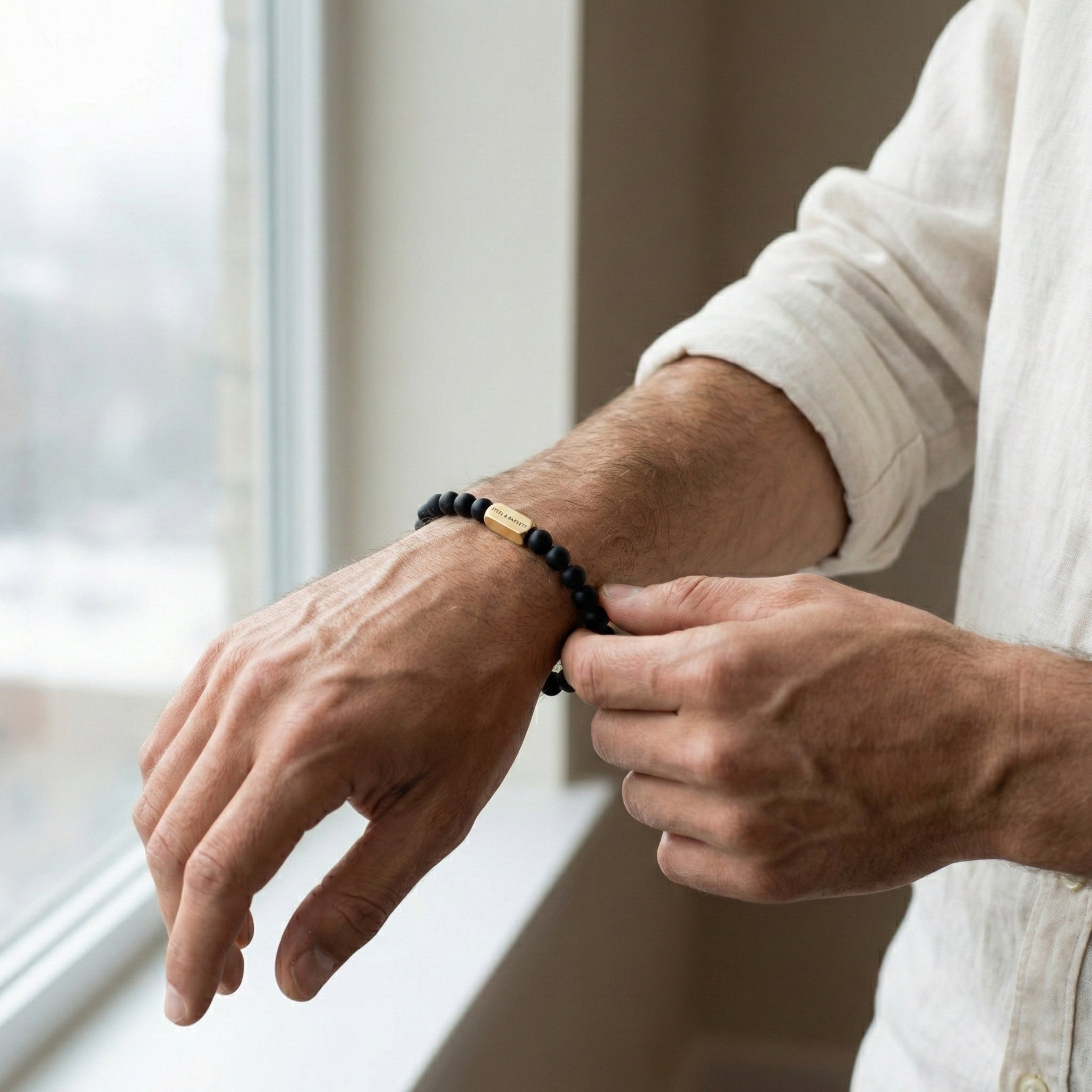 Black beaded men’s bracelet with matte beads and plated 18K gold clasp on dark stone surface