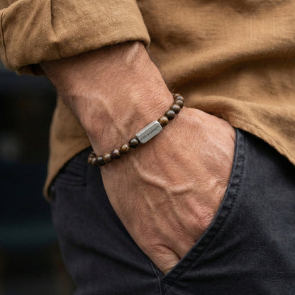 Bronzite beaded men’s bracelet with brown stone beads and brushed stainless steel bar worn on wrist with hand in pocket