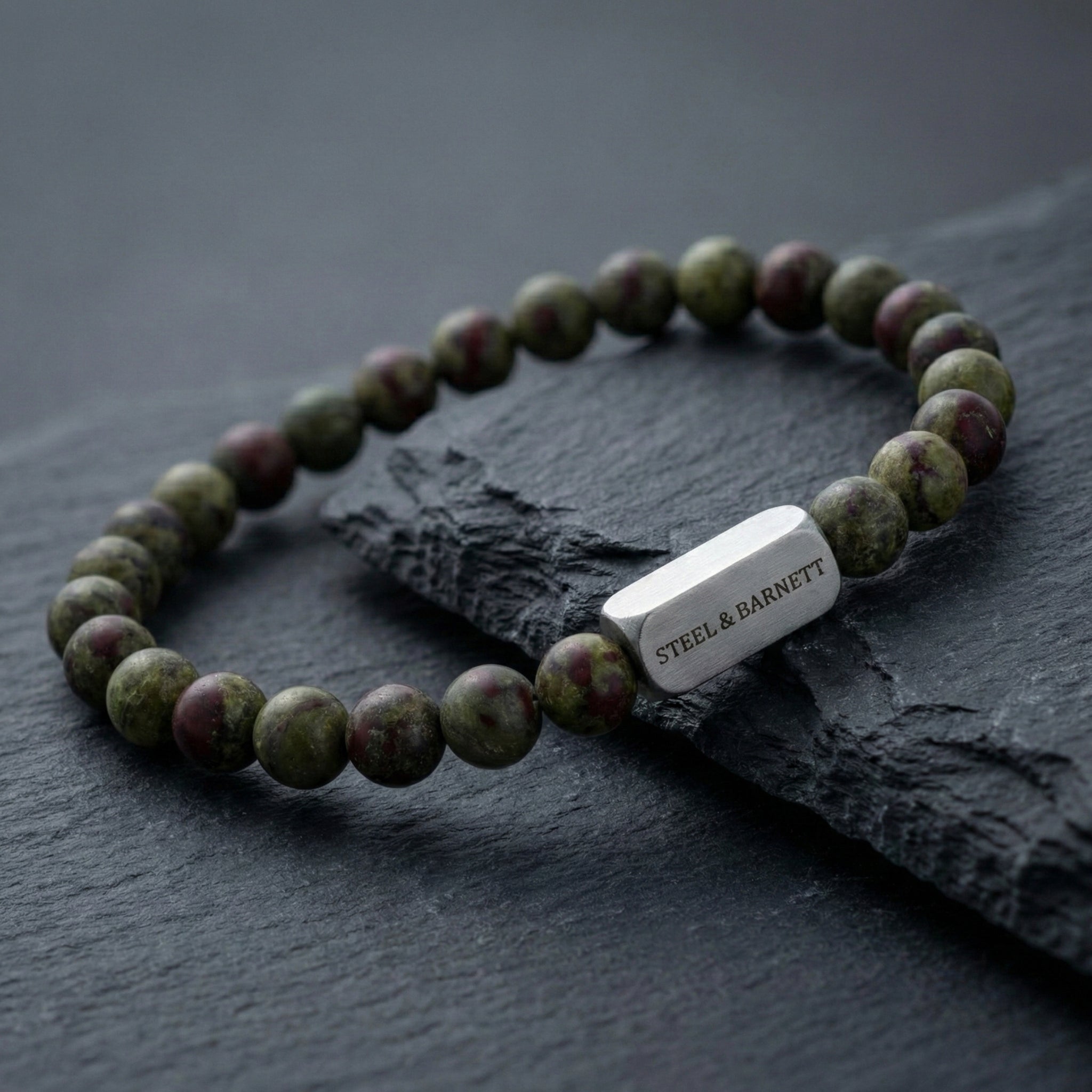 Dragon blood jasper men’s bracelet with round natural stone beads and brushed stainless steel bar on dark stone surface