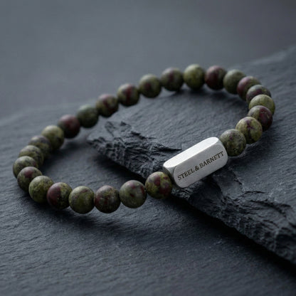 Dragon blood jasper men’s bracelet with round natural stone beads and brushed stainless steel bar on dark stone surface