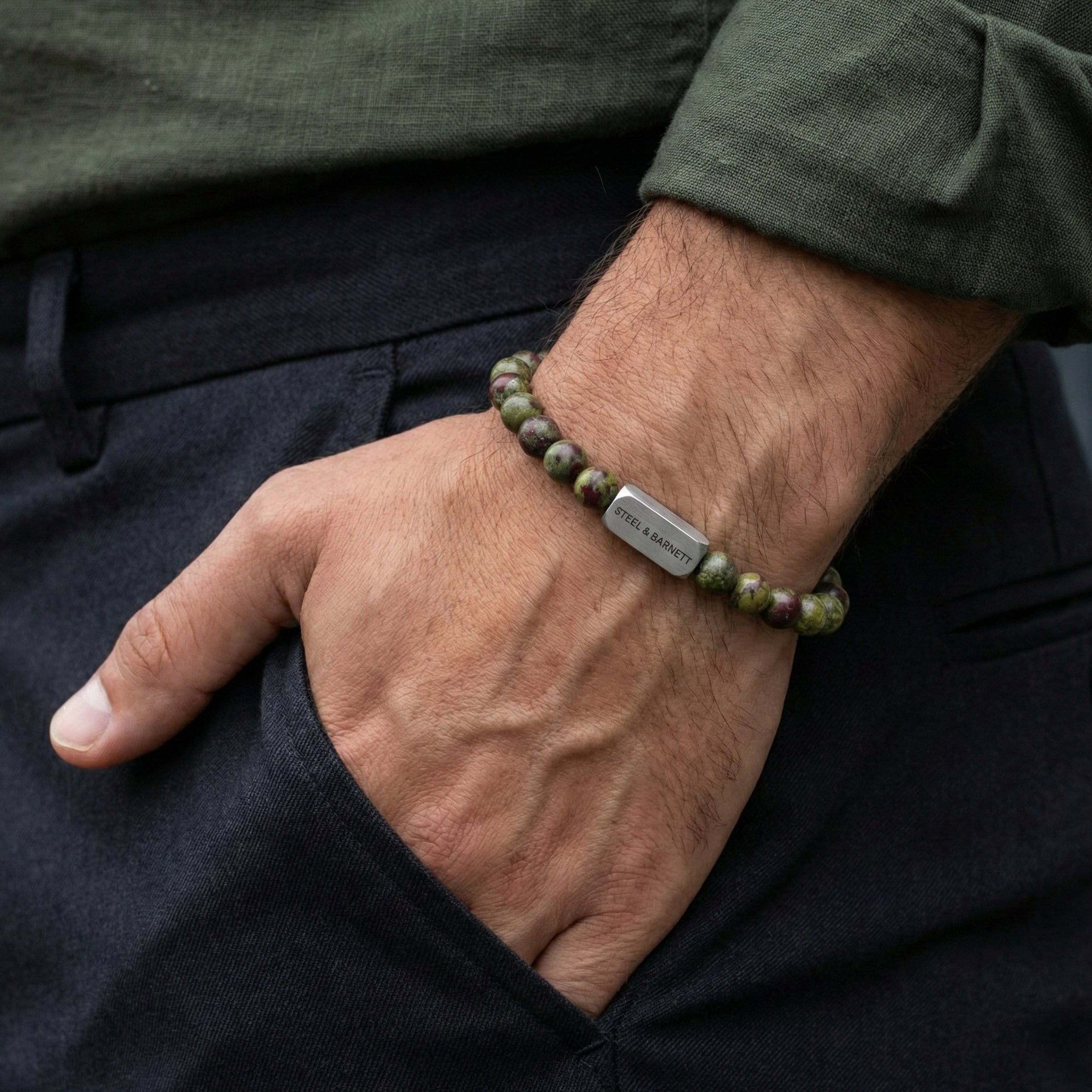 Dragon blood jasper men’s bracelet with green and red beads and brushed stainless steel bar worn on wrist with hand in pocket