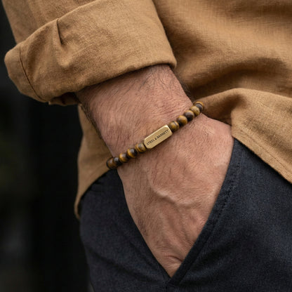 Tiger eye men’s bracelet with brown and gold beads and plated 18K gold clasp worn on wrist with hand in pocket