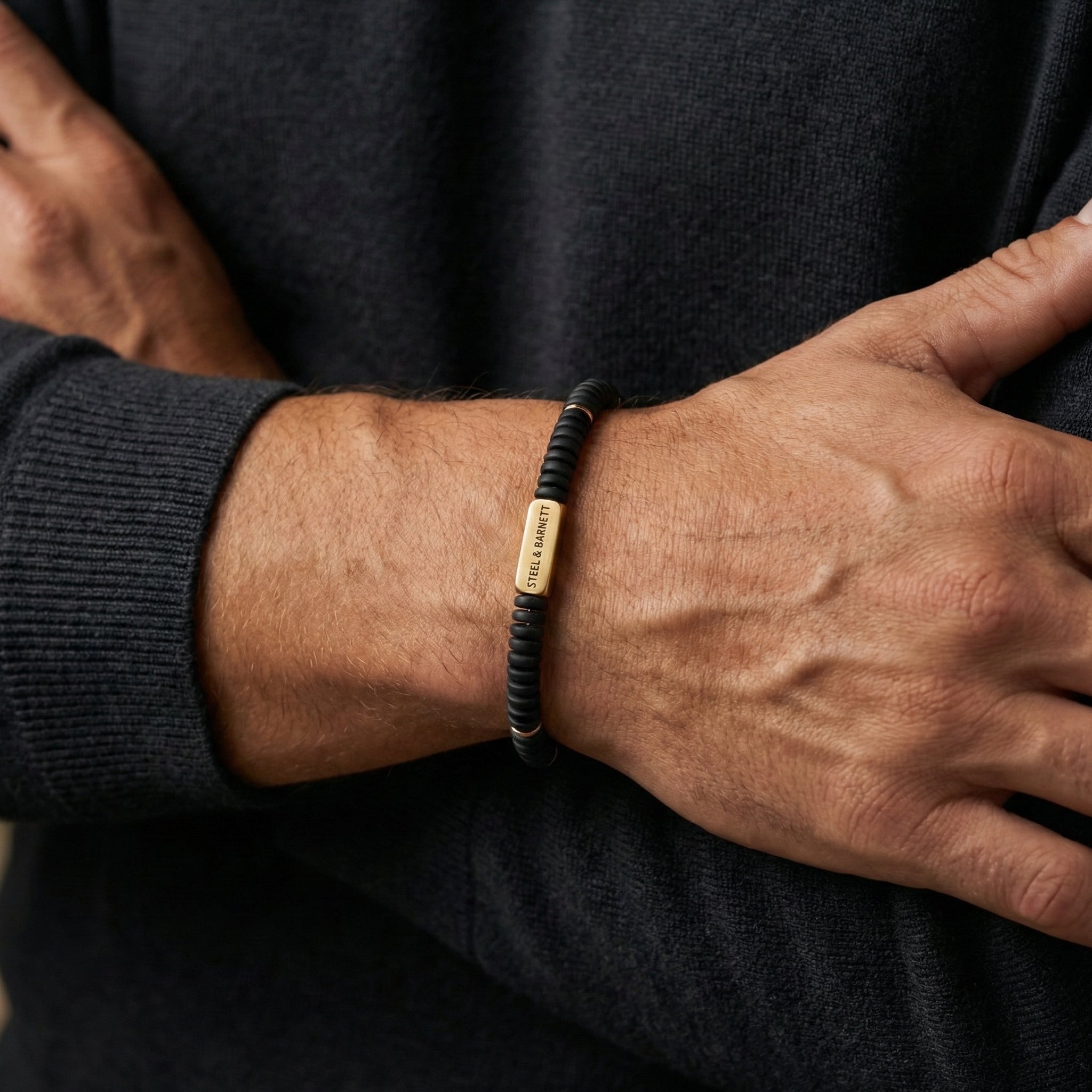 Black beaded men's bracelet with matte disc beads and rectangular plated 18K gold accent plate worn on wrist
