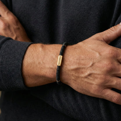 Black beaded men's bracelet with matte disc beads and rectangular plated 18K gold accent plate worn on wrist