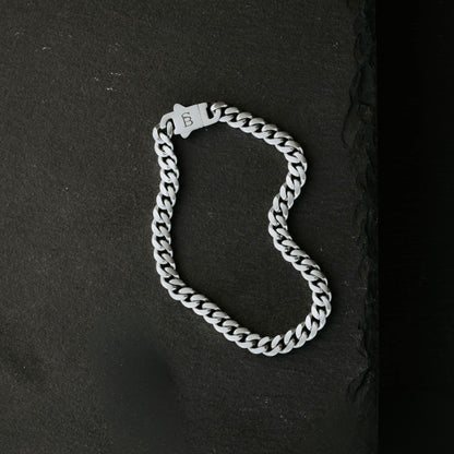 Silver toned stainless steel men’s bracelet with Cuban chain links and engraved clasp on dark stone surface