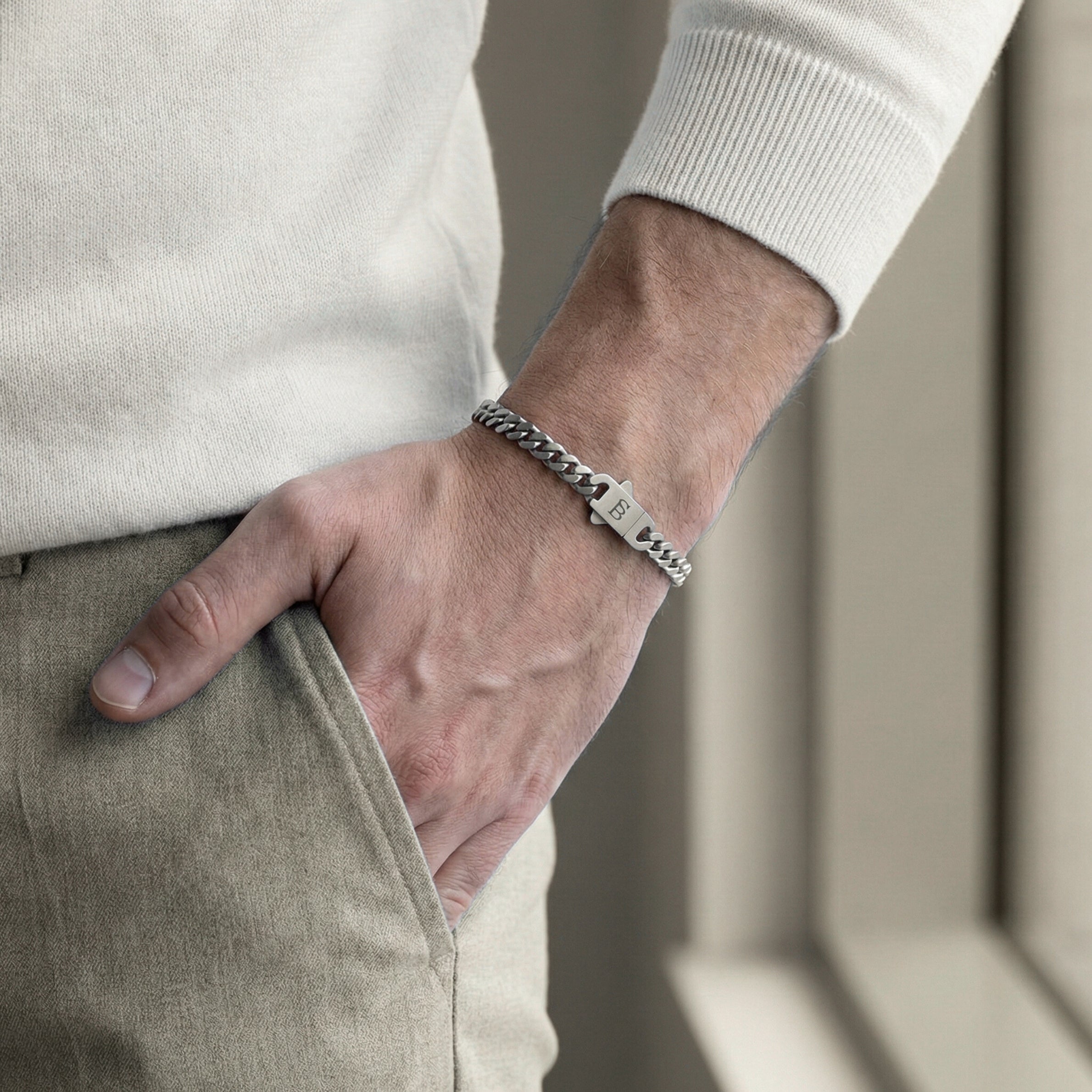Silver toned stainless steel men’s bracelet with Cuban chain links and engraved clasp worn on wrist with light sweater