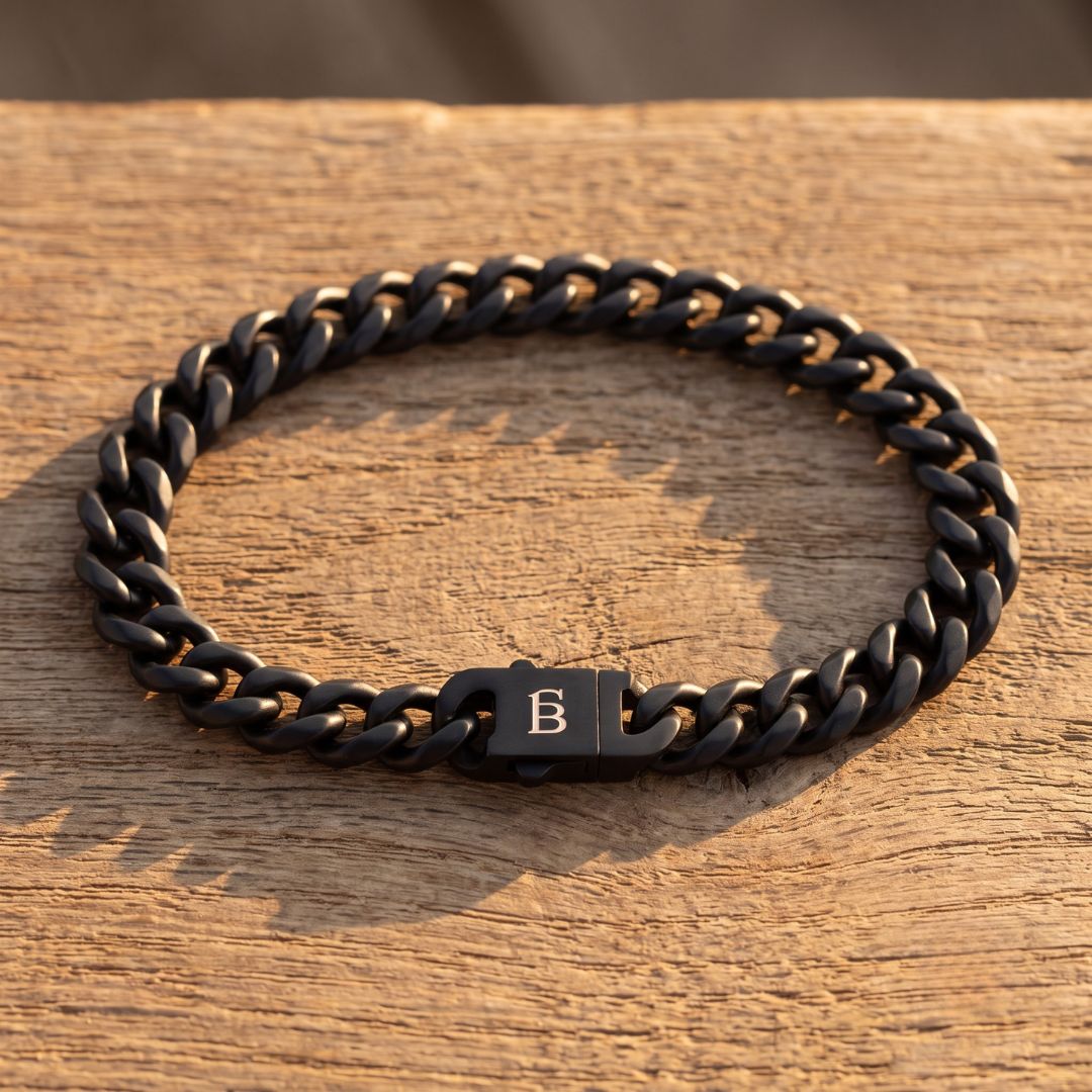 Black stainless steel men's bracelet with a curb chain design and engraved clasp displayed on a wooden surface
