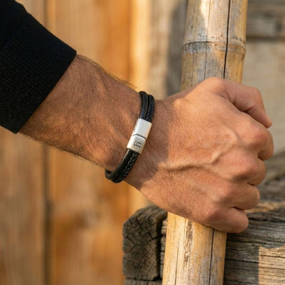 Black cowhide leather bracelet with braided and smooth bands and brushed stainless steel magnetic clasp worn on wrist outdoors