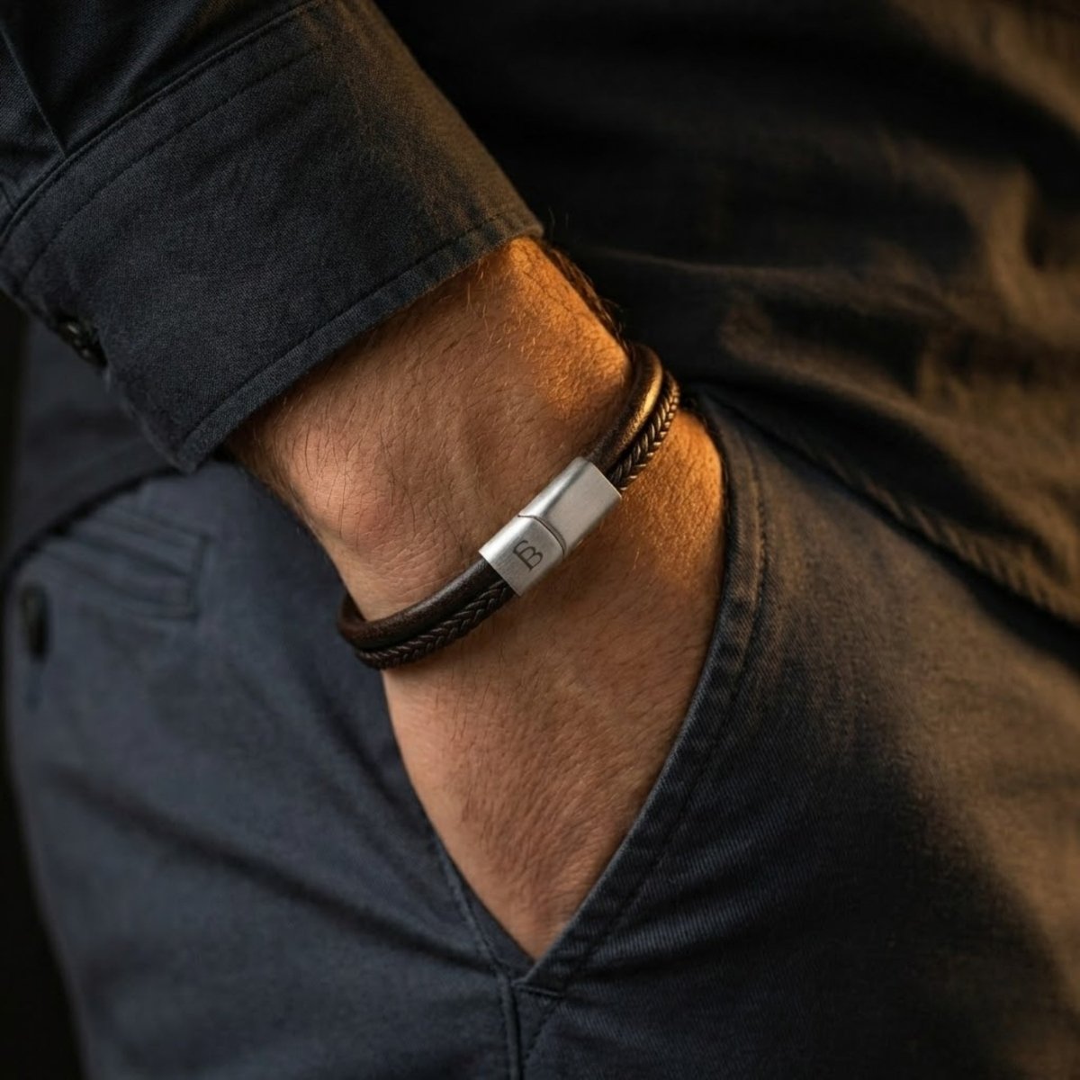 Brown braided leather men's bracelet with brushed stainless steel clasp worn on wrist with casual jacket sleeve